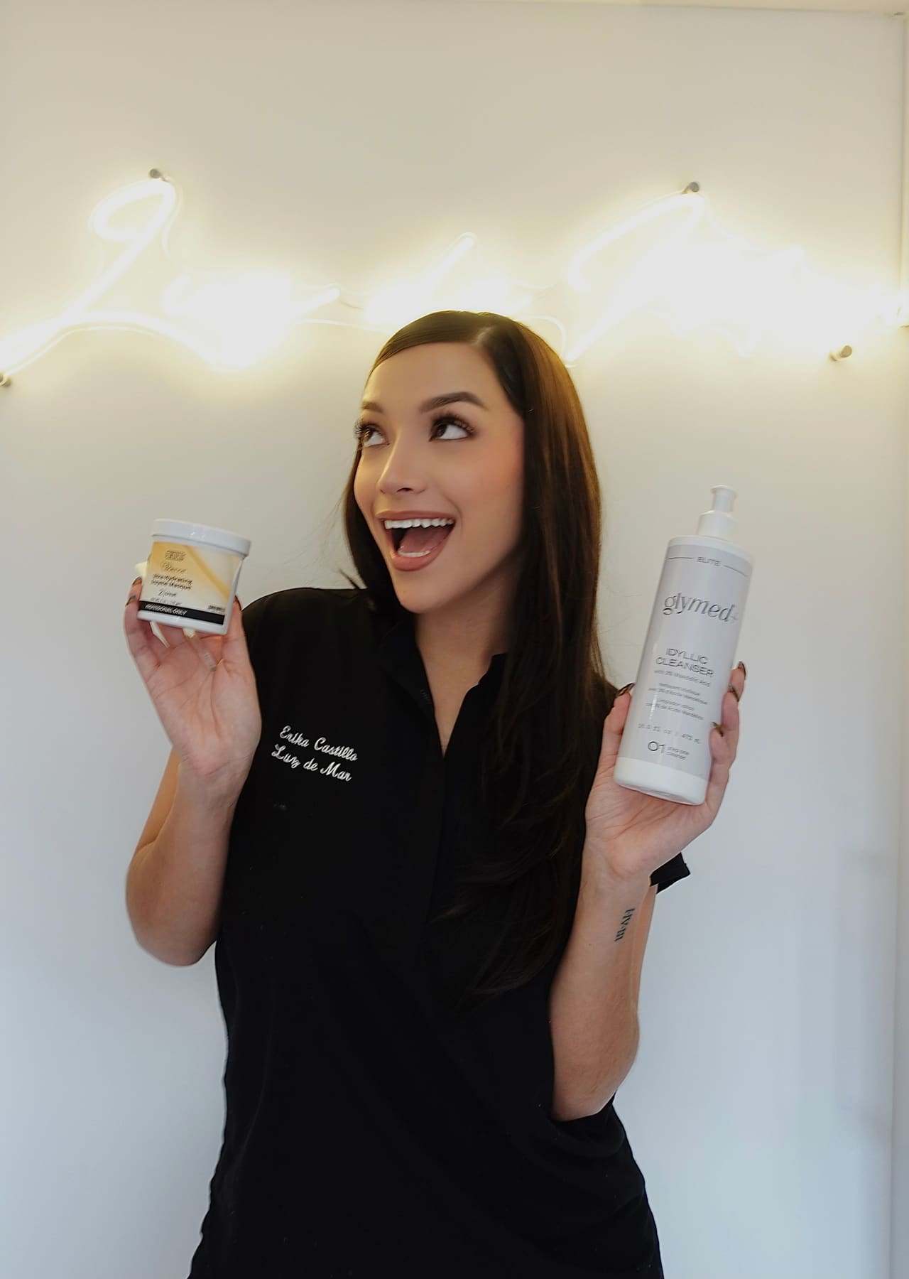 Erika Castillo holding professional skincare products beneath the Luz de Mar neon sign