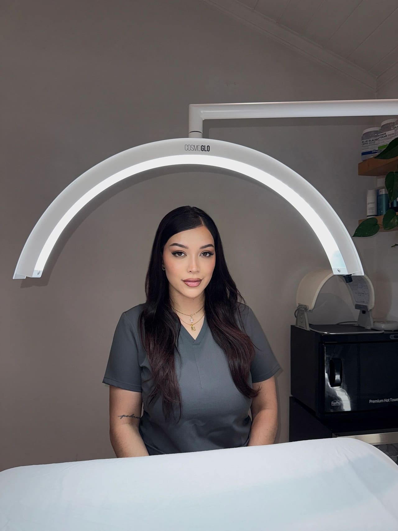 Erika Castillo in scrubs at the treatment bed, beneath the curved CosmoGlo treatment lamp