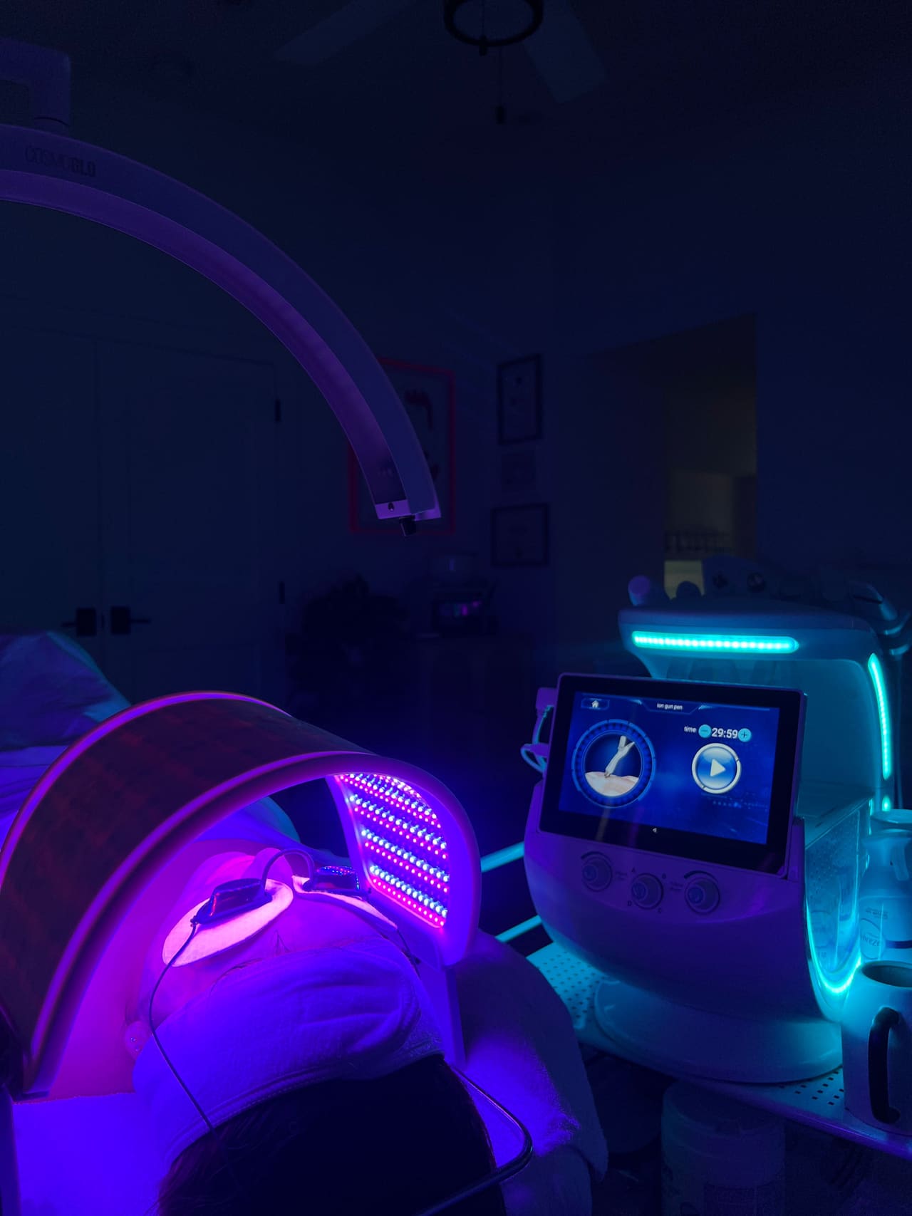A client under a folding LED light panel beside a multi-function facial machine in the dimmed treatment room