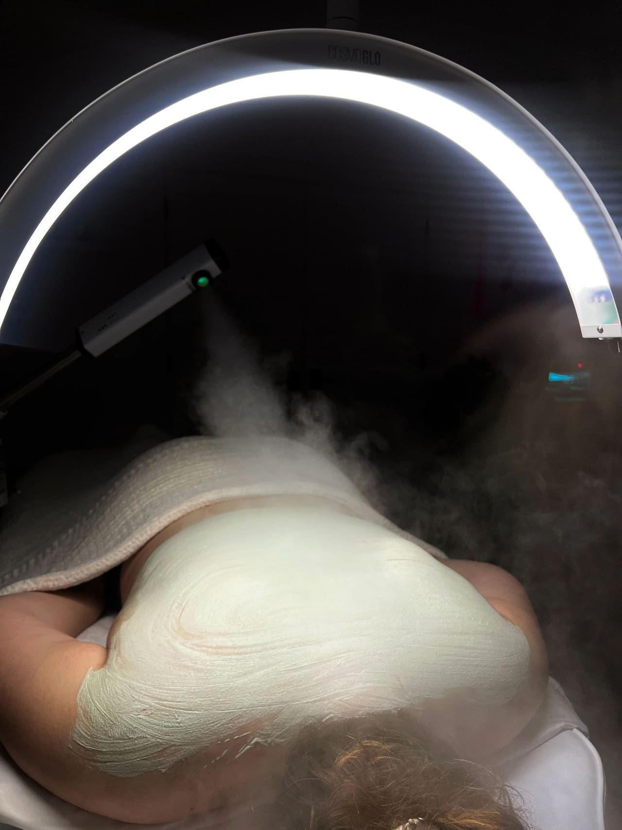 Steam drifting over a client during a mask treatment, lit by the curved treatment lamp