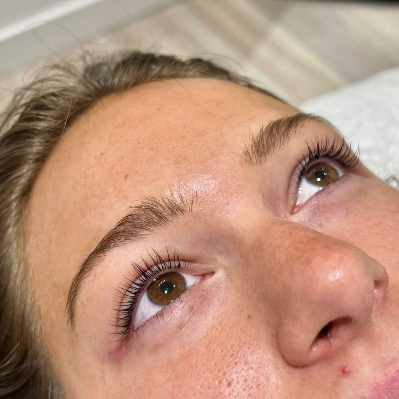 Close-up of a client looking upward, with dark, defined, curled lashes and brushed brows