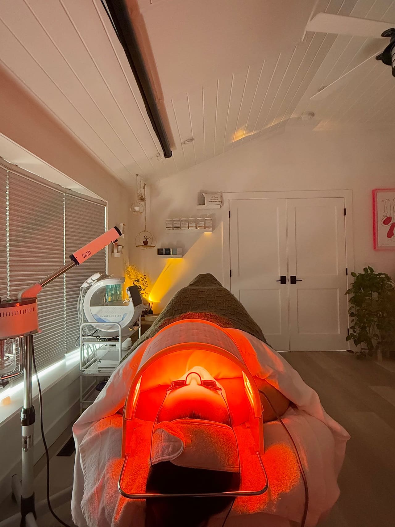 A client resting under a red LED light therapy mask during a facial at the Hampton Bays studio