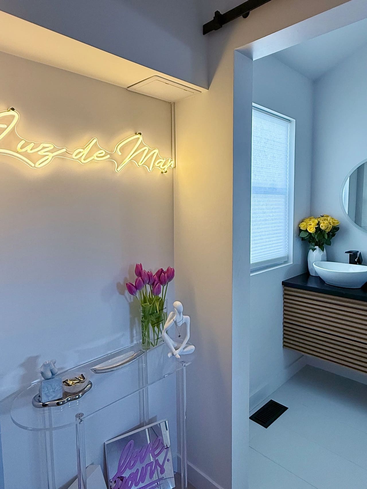 The entrance of the Luz de Mar studio — the gold neon sign, an acrylic console with fresh tulips, and the washroom beyond